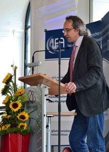 Herr Prof. Dr. Ludwig Fesenmeier, Vorsitzender der Trägervereinigung, steht am Rednerpult und spricht bei der Absolventenfeier im Sommer 2017. Vor dem Rednerpult steht ein Bouquet mit Sonnenblumen.